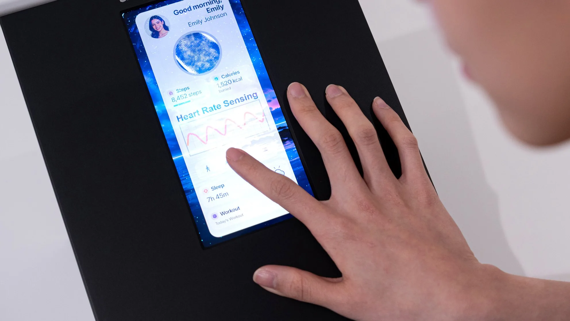 A hand touches a phone-sized Samsung Display OLED panel showing a heart-rate screen on a black demo stand