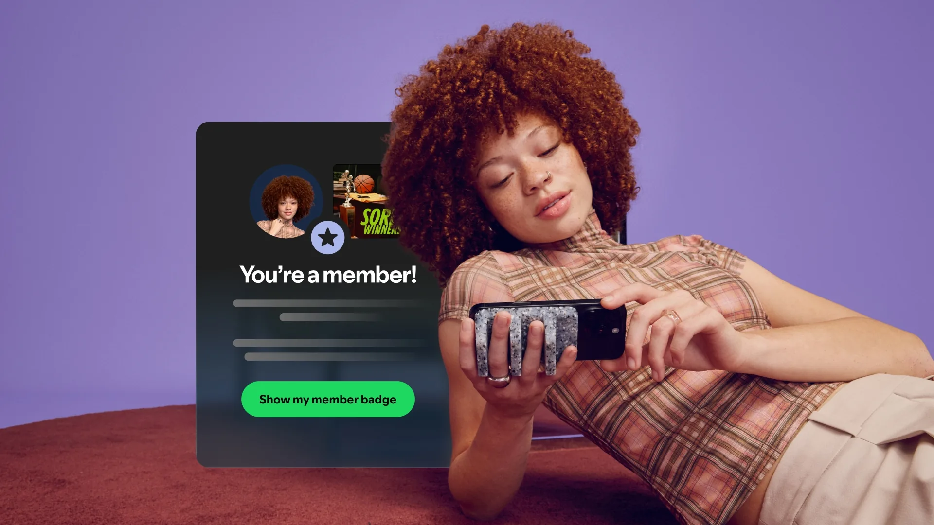 A woman with curly red hair lies back looking at her phone, beside a Spotify pop-up reading "You're a member!" with a Show my member badge button