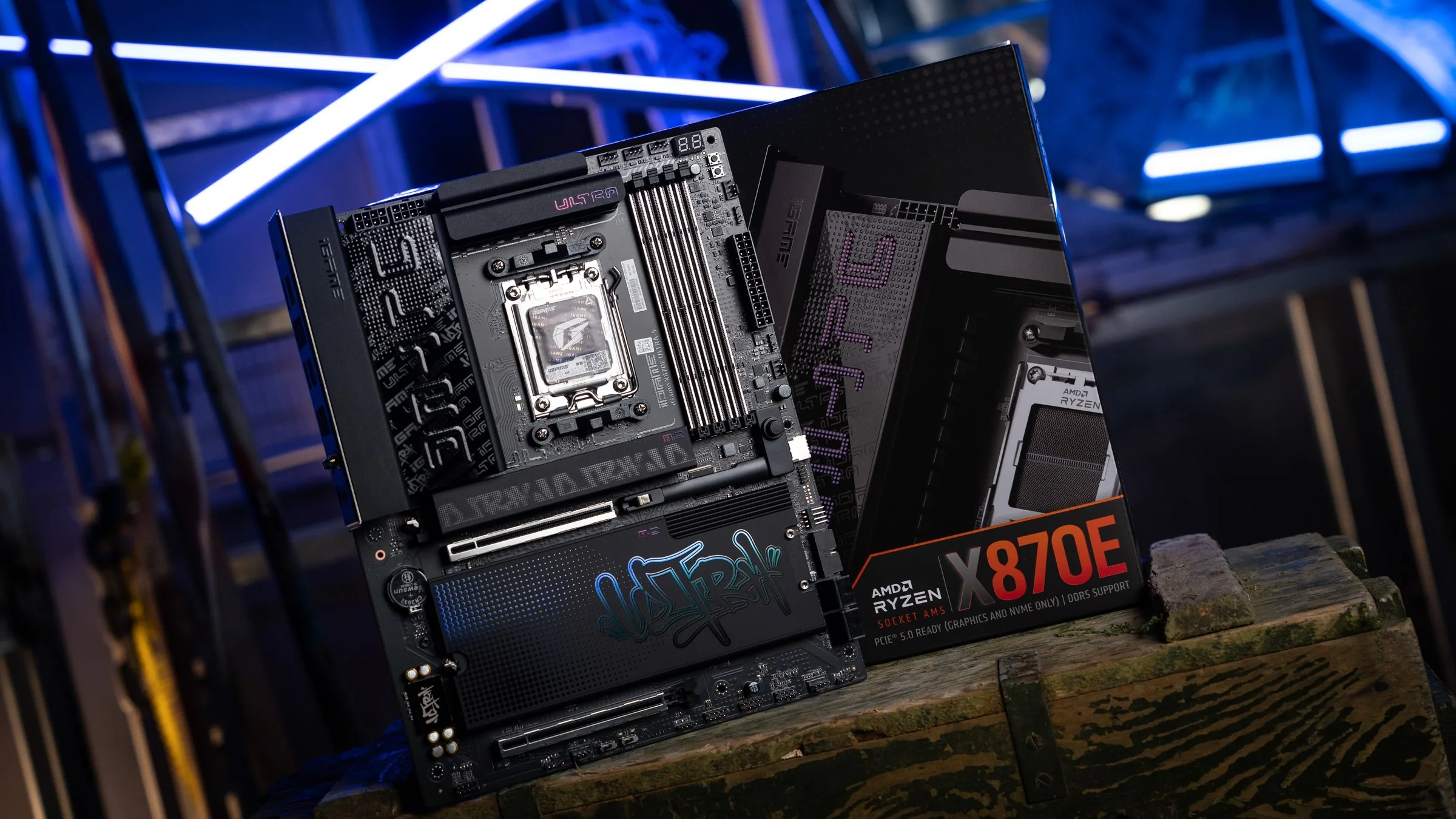 A black Colorful iGame X870E Ultra-S V14 motherboard with graffiti-style lettering on its heatsinks, leaning against its retail box under blue neon lights