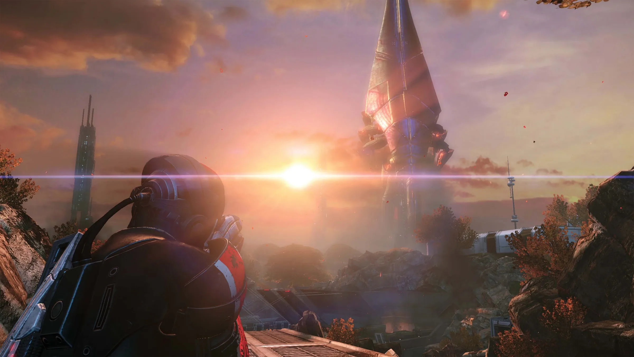 An armored soldier, seen from behind, looks toward a towering alien ship at sunset in Mass Effect Legendary Edition