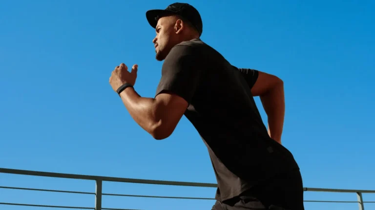 A man in a black cap and black T-shirt runs against a blue sky, wearing a black Fitbit Air band on his wrist