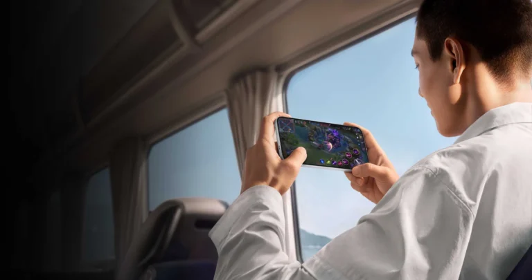 A man in a white shirt plays a game on an Oppo Find X10 Pro Max held sideways, seated by a window