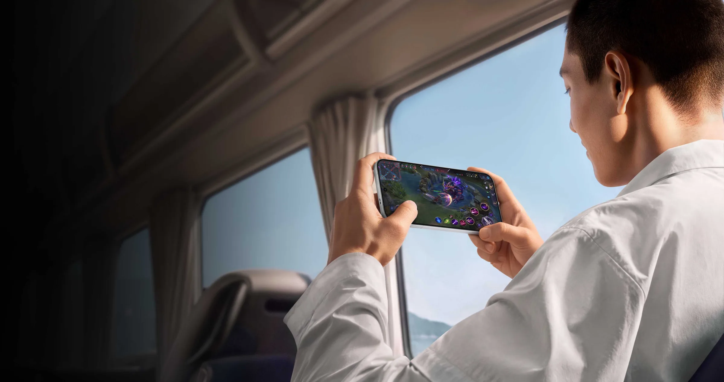 A man in a white shirt plays a game on an Oppo Find X10 Pro Max held sideways, seated by a window