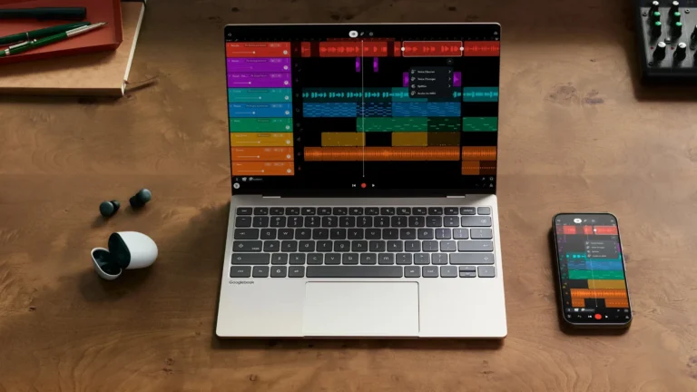 A silver Googlebook laptop on a wooden desk beside a phone, both showing the same multitrack music app, with earbuds and an audio mixer nearby