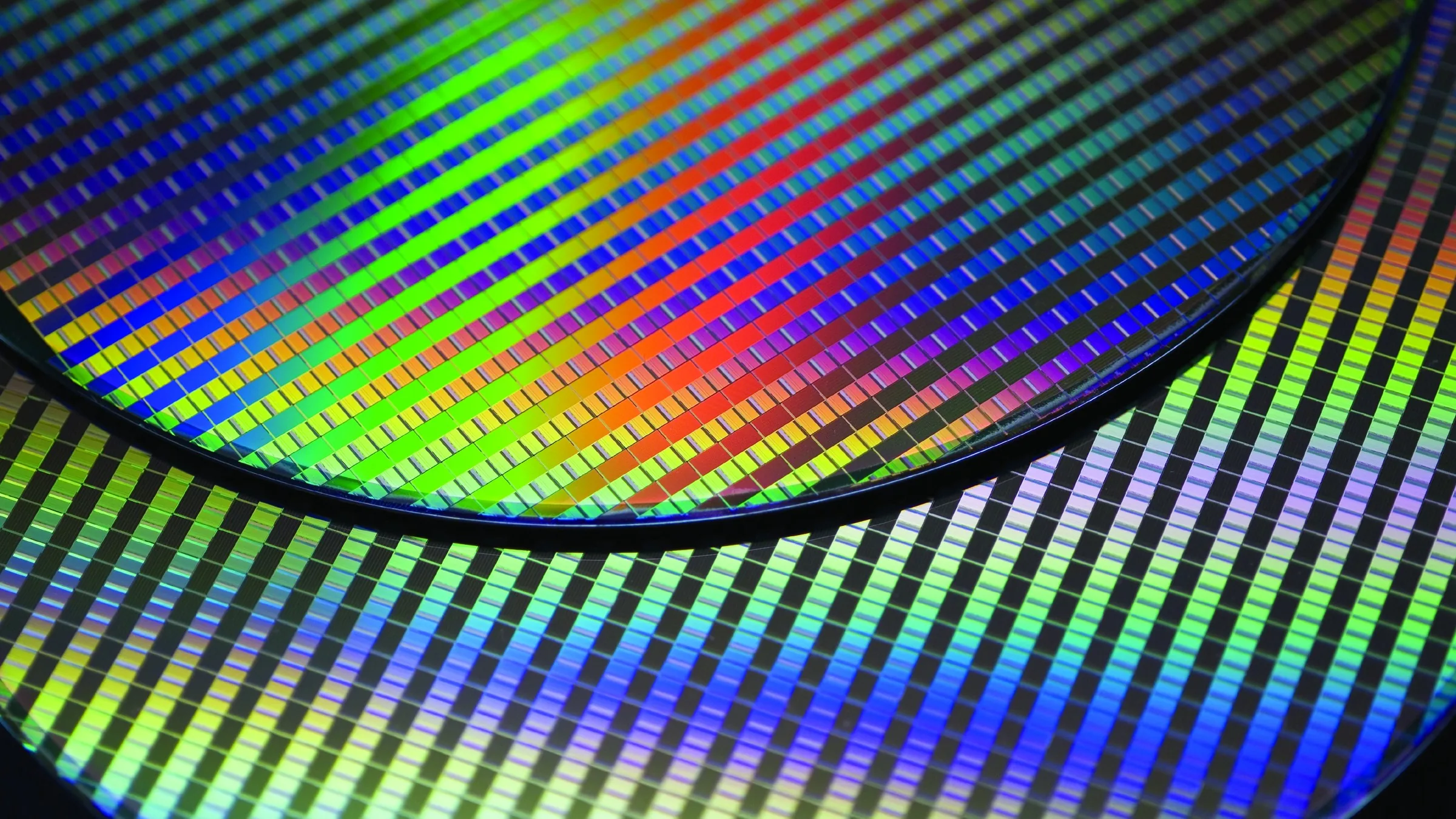 Close-up of two silicon wafers patterned with rows of chips, reflecting green, blue, red and orange light