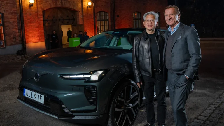 NVIDIA CEO Jensen Huang and Volvo Cars CEO Håkan Samuelsson standing beside a dark green Volvo electric SUV outside a brick building at night